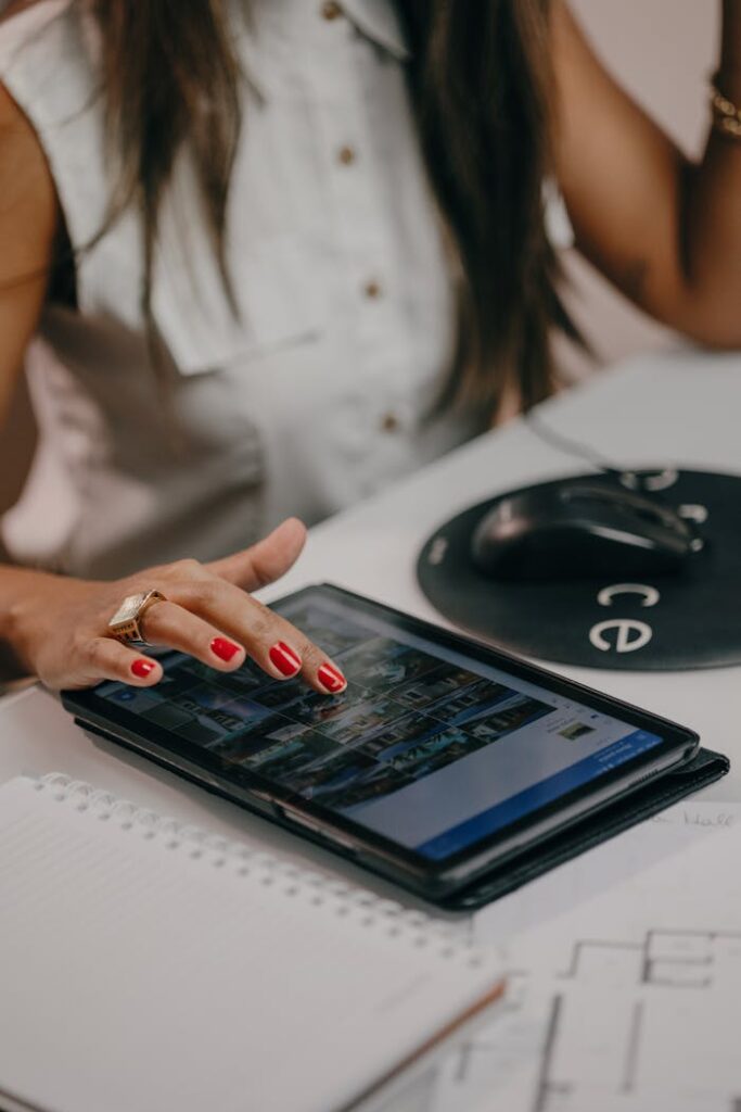 A woman with manicured nails uses a tablet on a desk, technology in focus.